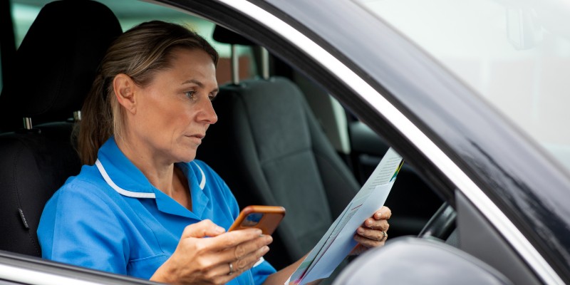 Nurse sits in car holding phone and paperwork and looking concerned
