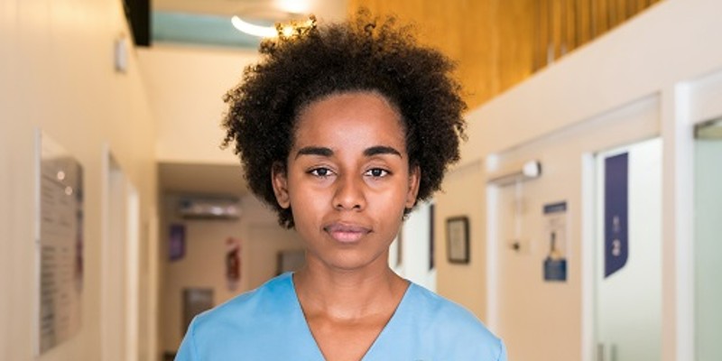 Tired nurse in scrubs in a hospital corridor looking straight at camera