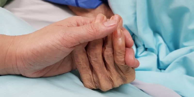 Close up of a nurse's hand holding onto an elderly patient's hand