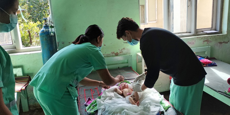 two nursing staff with a baby in a basic overseas ward