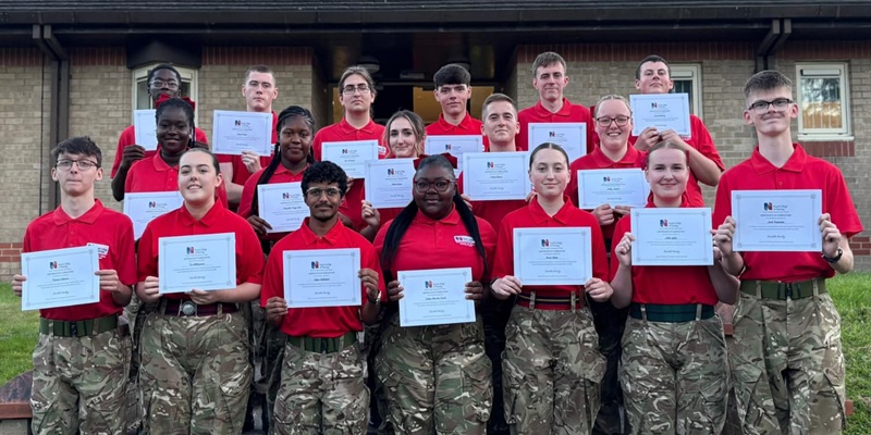 A group of cadets in uniform, holding their certificates and smiling at the camera