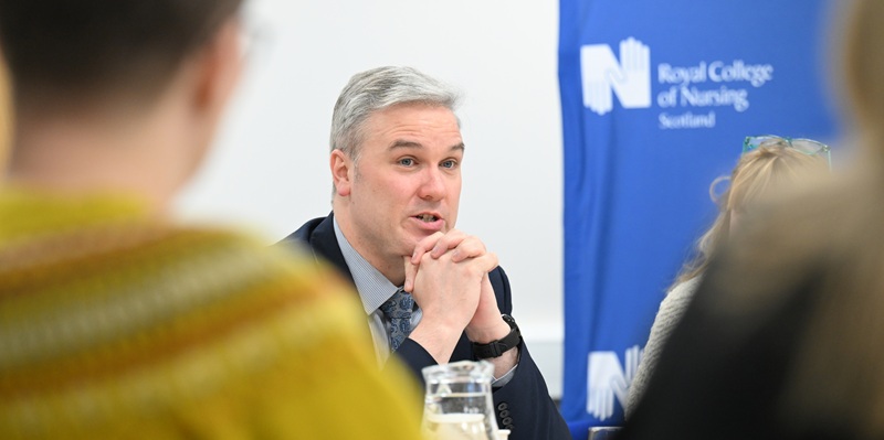 Tom Arthur in speaking with RCN Scotland logo in the background