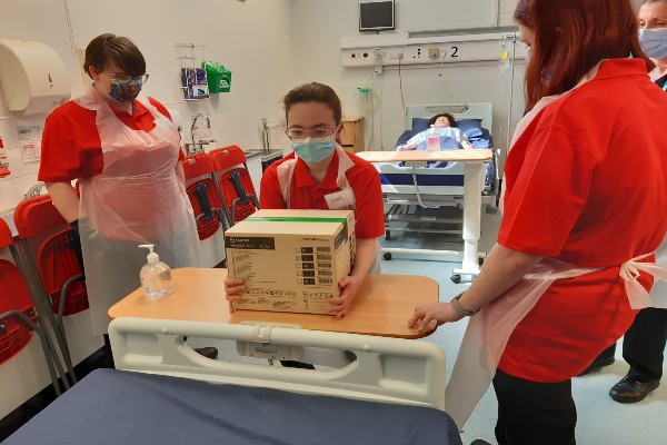 A group of cadets in red shirts in a clinical setting lifting boxes. 