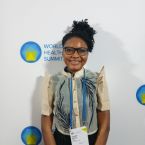 A woman wearing an orange jacket speaks into a microphone