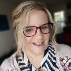 Kirsten Bland, Dorset member of the South West regional board, with blonde wavy hair and glasses, smiling athe the camera wearing a black and white striped shirt and flowery pink cardigan