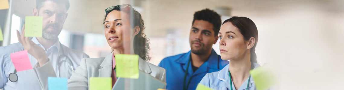 Nurse educator teaching three other healthcare professionals, placing post it notes on a glass screen