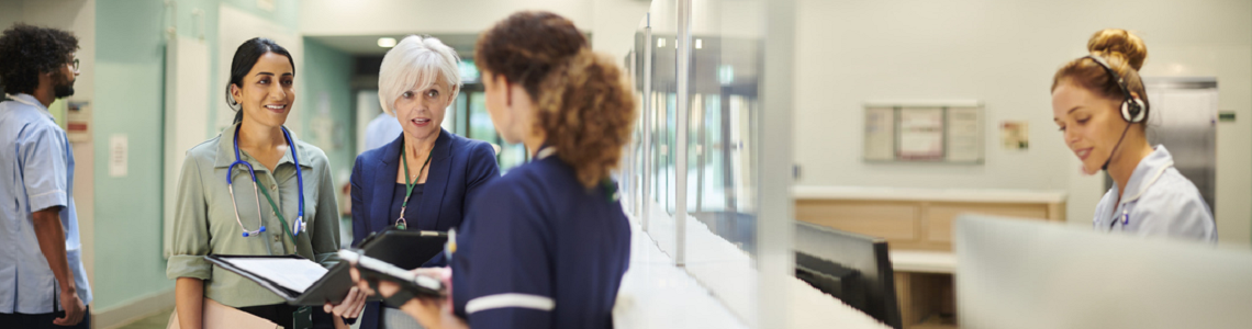 A nurse manager holding a folder talking with a doctor and another senior nurse at a nursing station