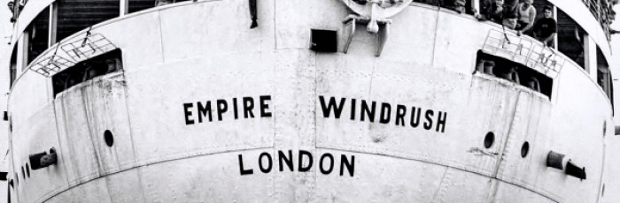 Old black and white photo of a ship full of people. Written on the front of the boat is "Empire Windrush London"