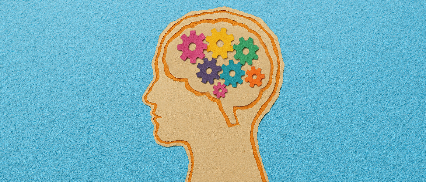 A scrapbook-style illustration of a human head in profile, with the brain area filled with small, paper cogs in a variety of bright colours. 