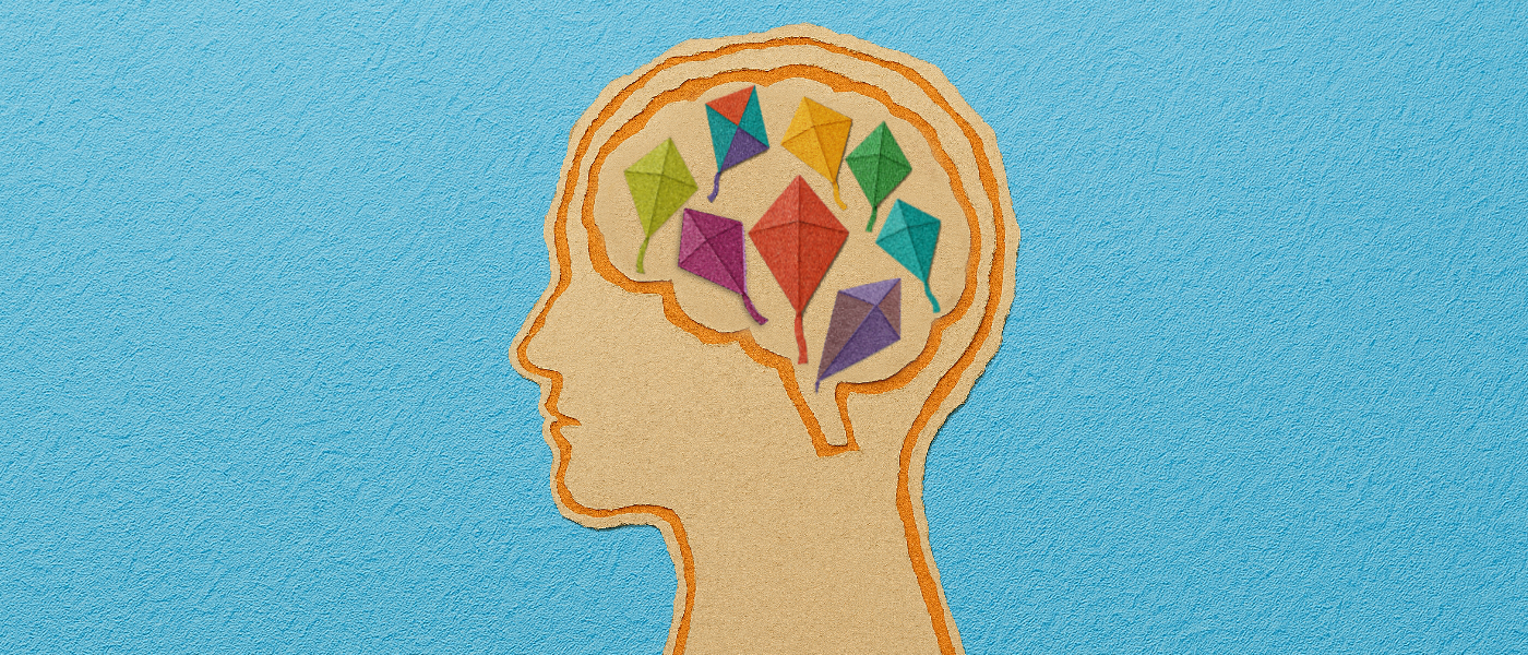 A scrapbook-style illustration of a human head in profile, with the brain area filled with small, origami kites in a variety of bright colours. 