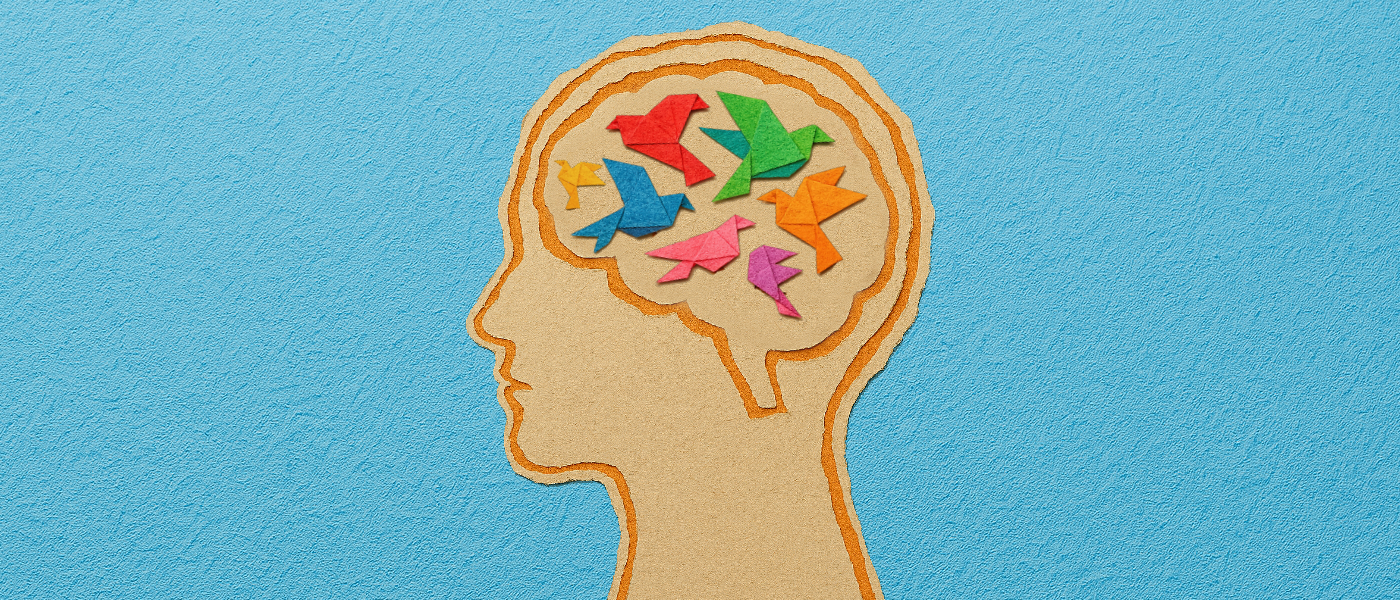 A scrapbook-style illustration of a human head in profile, with the brain area filled with small, folded paper birds in a variety of bright colours. 