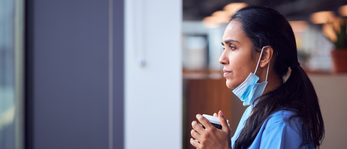 Female nurse holding a coffee cup looking pensive, staring out a window