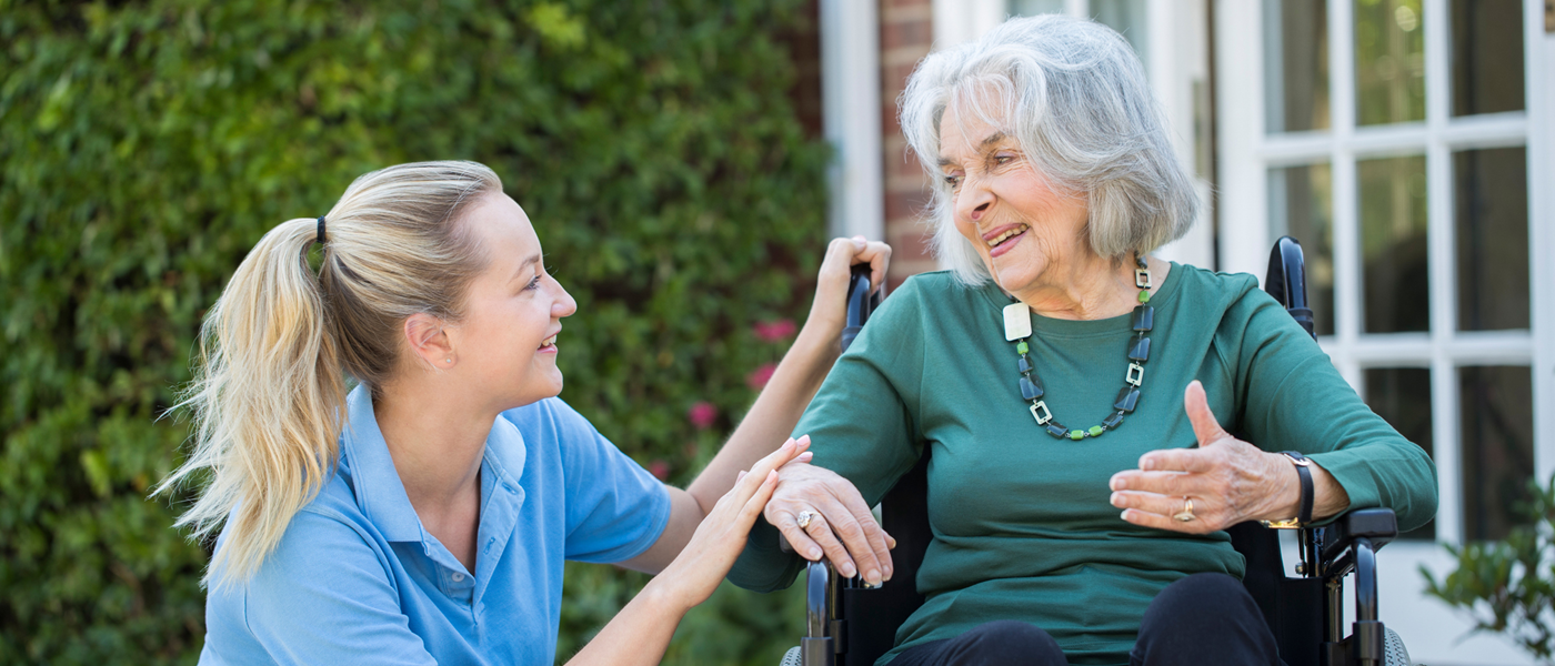 A female nurse squats down to speak to lady in a wheelchair outside a care home