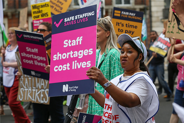 A nurse holding a sign that says Staff shortages cost lives