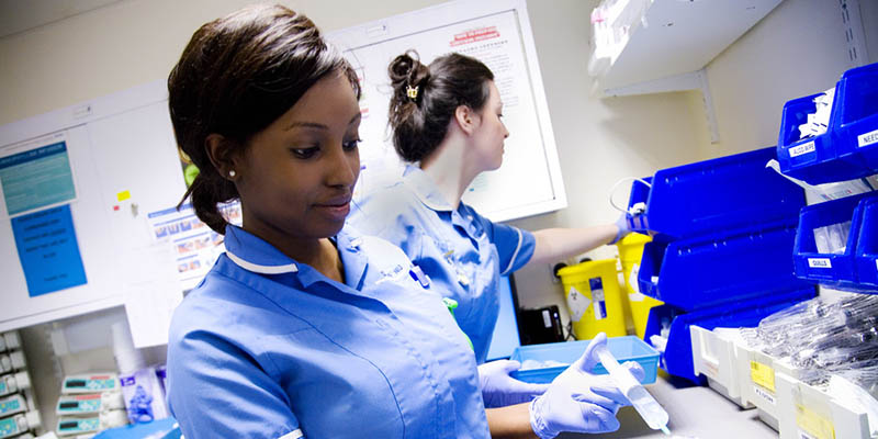 Two female staff nurses organising medicines on an acute ward - one black, one white Two female staff nurses organising medicines on an acute ward - one black, one white