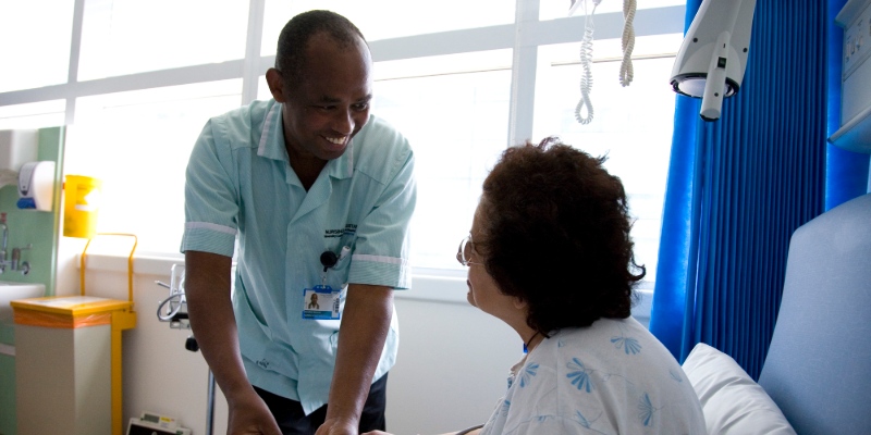 Smiling nursing assistant speaks with patient in hospital bed