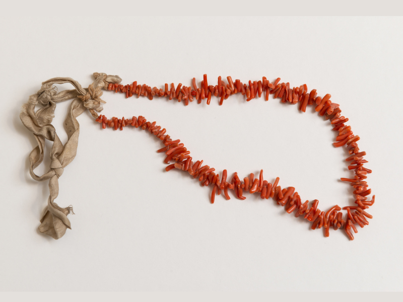 photo of a necklace with coral coloured stones and an attaching ribbon