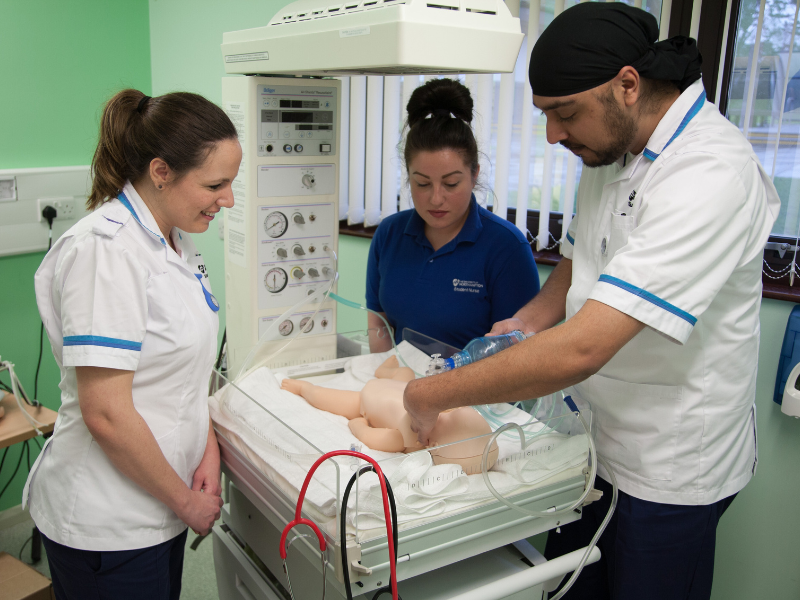 three nurses on a hospital ward, doing nursing training on a pretend baby