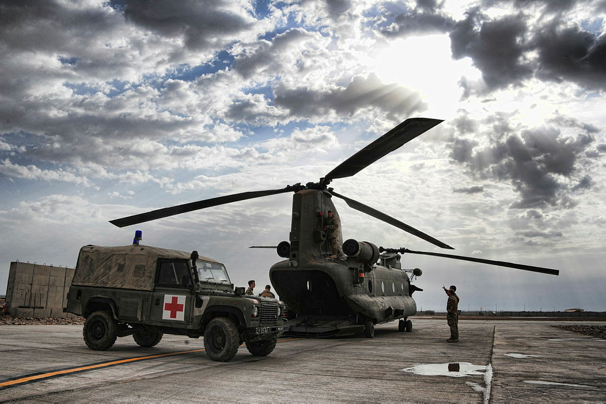 And ambulance truck with a red cross printed the side parked next to a Chinook helicopter