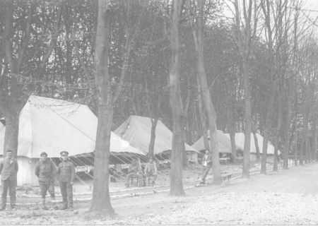 Black and white photograph of people in uniform in casual poses, standing outside 3 white tents. 