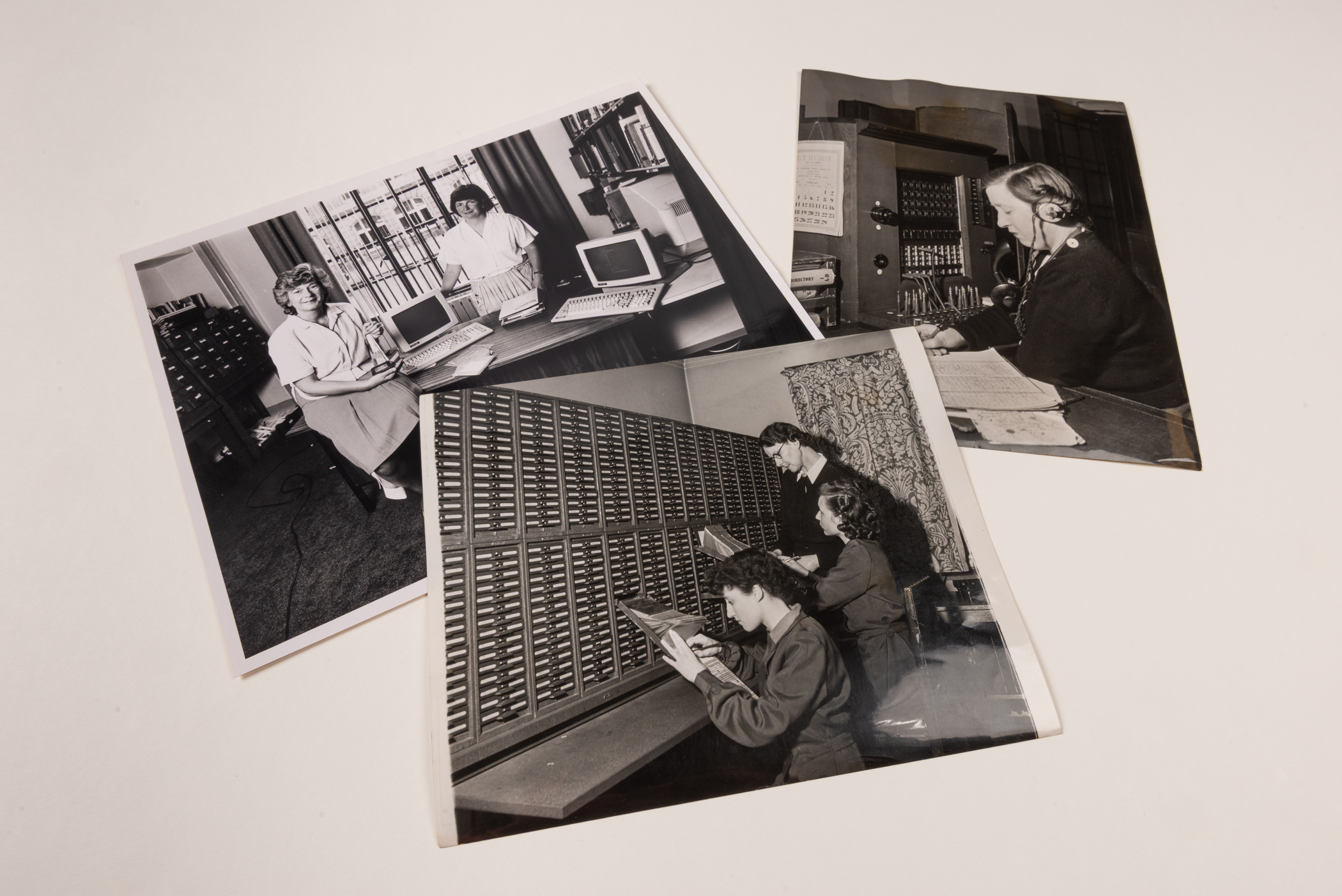 Three overlapping, black and white photographs showing two librarians posing beside a desk with old computers, three clerks pulling documents from a wall of wooden drawers, and a switchboard operator wearing headphones and taking notes.