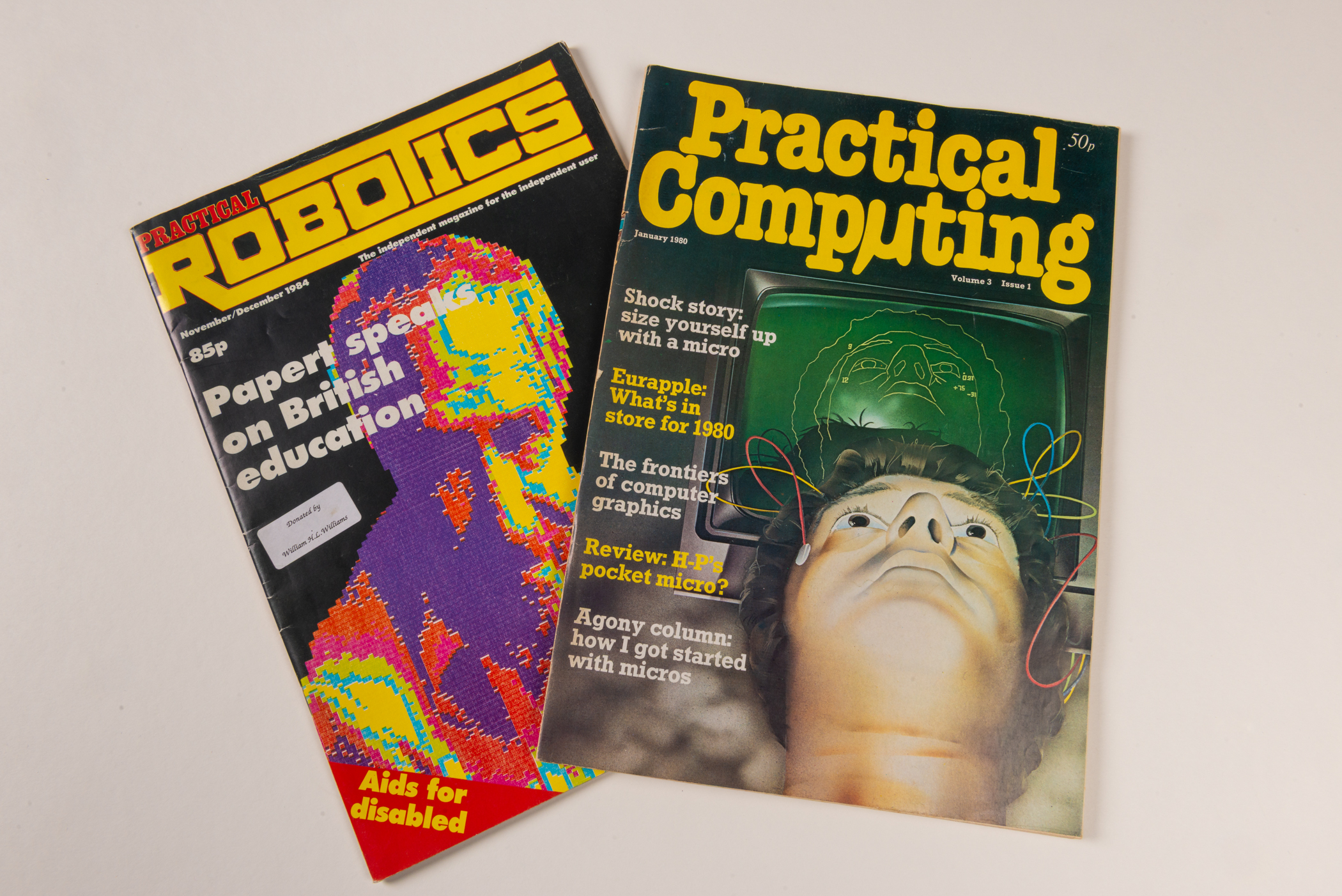 Two overlapping magazines with bright yellow titles. Practical Robotics shows a multi-colour graphic of a person's head and shoulders. Practical Computing shows a person's head with wires attached at the temples leading to a green computer screen behind.