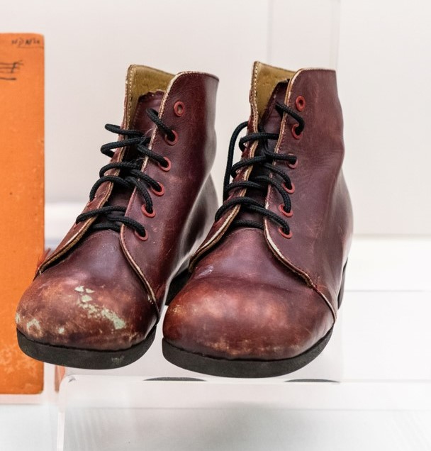 A pair of brown leather boots, with black laces. The tips are scuffed and they look well worn.