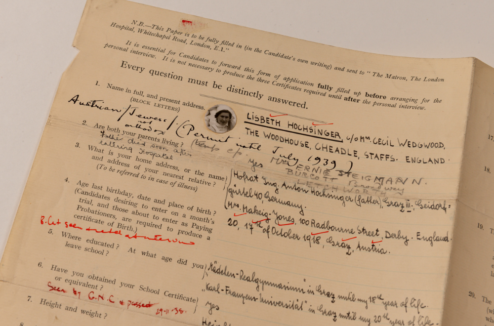 Close-up of an historic, typed, application form filled out by hand by Lisbeth Hochsinger. It includes a small black-and-white photo of her, red and black ink annotations, and grey pencil notes.