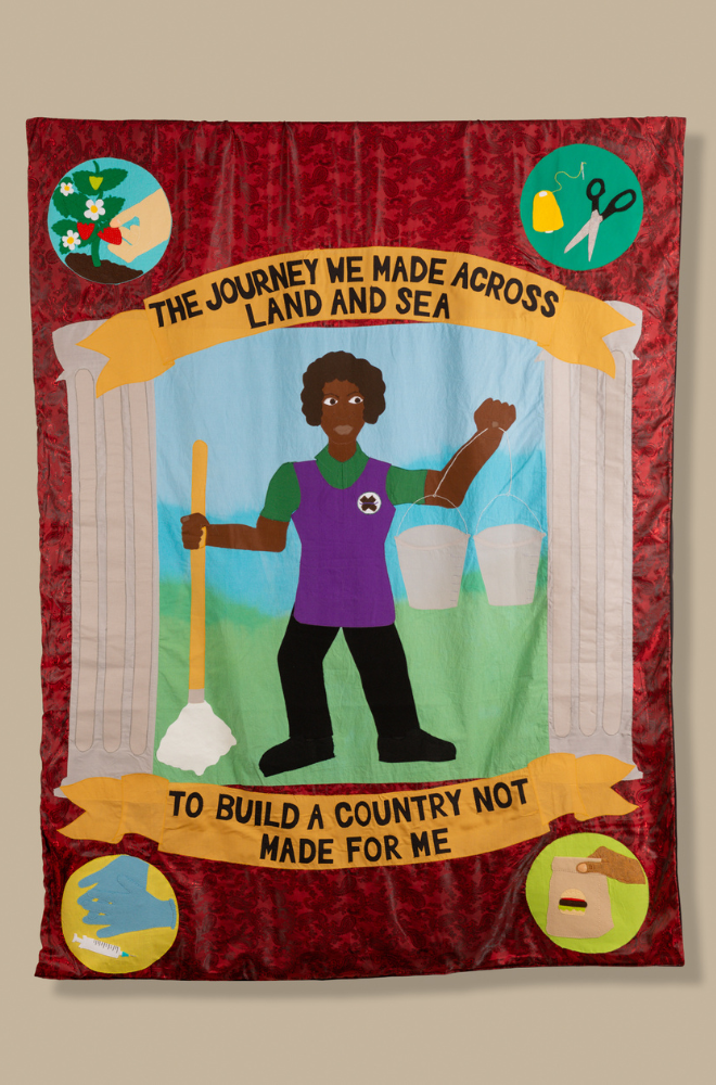 A vibrant, red textile banner with two white columns and a sky and grass background featuring a black woman wearing a green top, black trousers and a purple tunic holding a mop and two metal buckets. There are two yellow sashes above and below with text reading 'The journey we made across land and sea (top) to build a country not made for me (bottom)'. In each corner of the banner are four colourful roundels depicting a type of work sector; the top left shows a strawberry plant with a hand picking the fruit, top right shows a pair of scissors and yellow cotton, bottom right shows a hand holding a fast food bag and bottom left shows a pair of hands wearing blue sterile gloves and a syringe.