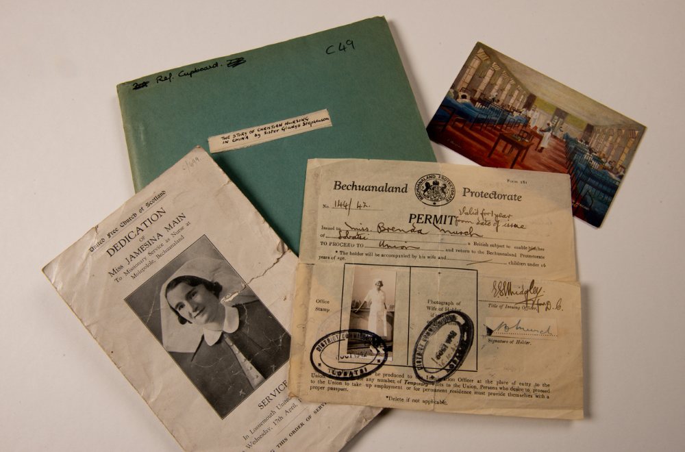 Four overlapping paper items including a green-blue book with a small, handwritten title 'THE STORY OF CHRISTIAN NURSING IN CHINA by Sister Gladys Stephenson', a church service programme for Miss Jamesina Main, a 'Bechuanaland Protectorate' permit, and a small, colour postcard showing ward with patients and nurses in the hospital for Africans, Accra, Gold Coast.