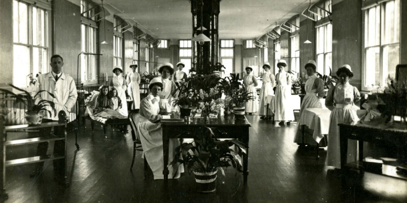 Black and white postcard image of the interior of a diptheria ward at Leeds City Hospital, Seacroft. The portrait contains nurses, doctors and two child patients.