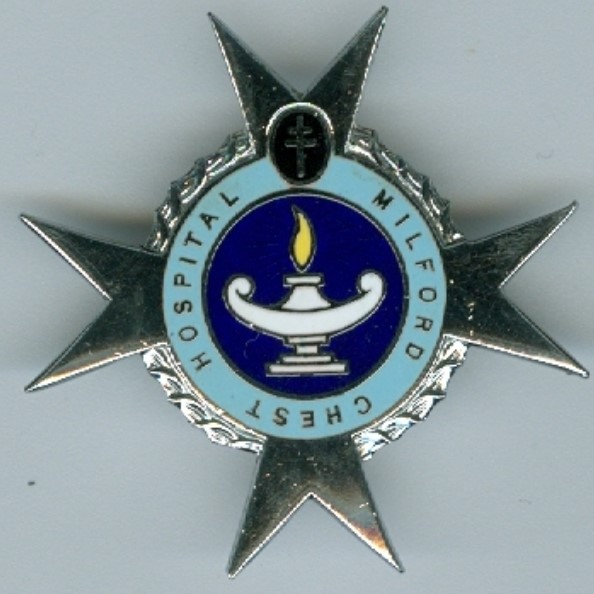 An enamel on silver badge with a central dark blue background with a Florence Nightingale style lamp, surrounded by a light blue circular banner with the name 'Milford Chest Hospital '. These then sit on a silver St John's cross. 