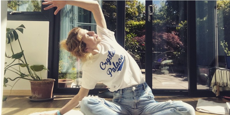 Woman in white t-shirt and jeans stretching in front of open French window 