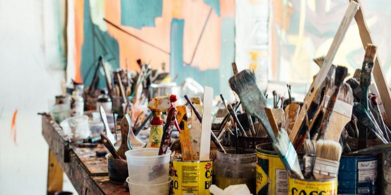 An image of several paint brushes and other art supplies on a table.