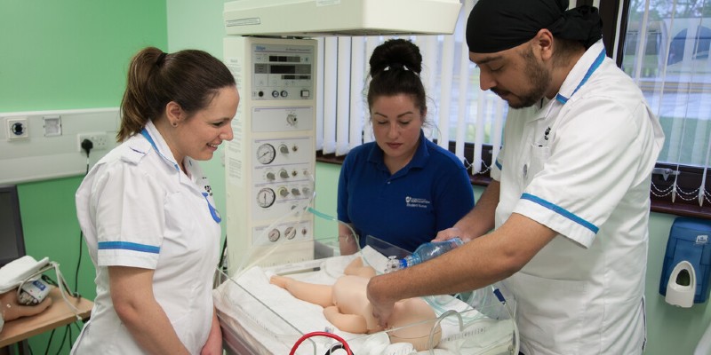 Student nurses and teacher working on a mannequin baby in a simulated ward environment