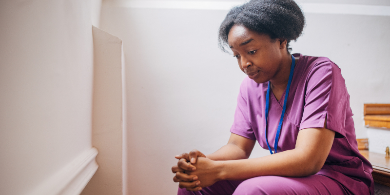 Nurse in scrubs sitting on a stair step looking burnt out
