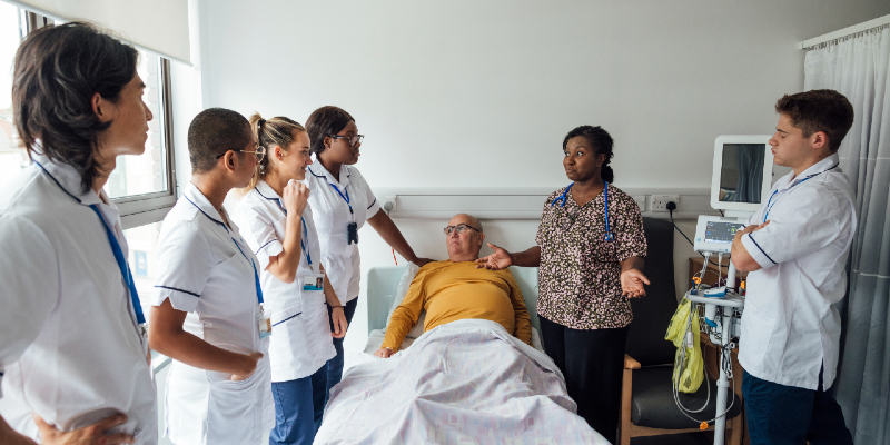 Group of nursing students gather around a hospital bed