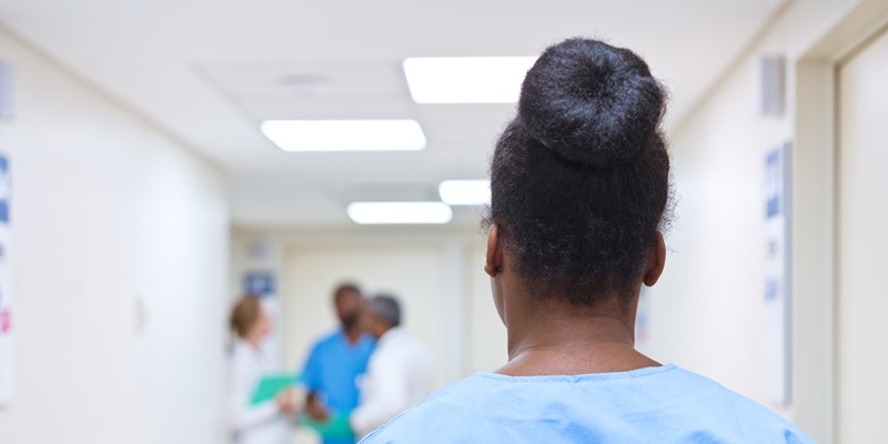 Back of nurse head with black hair tied in bun along hospital corridor
