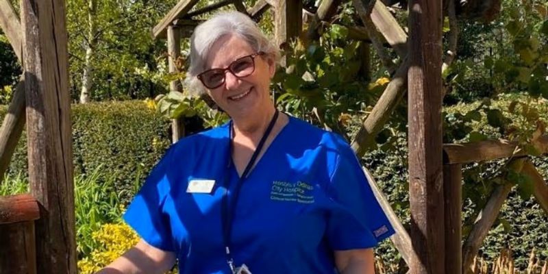 Terri Gazi, dressed in blue scrubs, stands underneath a garden arch