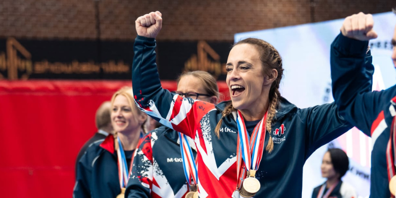 Powerlifter Delyth - white woman with long hair in plaits - is pictured celebrating with medals around her neck and arms up in the air