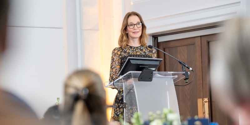 Writer, broadcaster, lexicographer and etymologist Susie Dent appears at a lecturn hosting the RCN Awards 2026 at RCN headquarters in London. She wears glasses, and a black dress with orange and white floral patterns