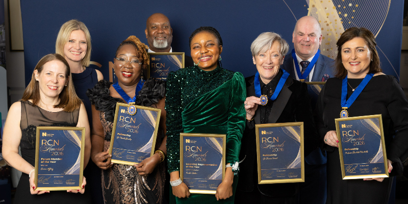Eight people are shown at the RCN Awards 2026. They are all winners, holding their placards and awards, and smiling, looking directly into the camera