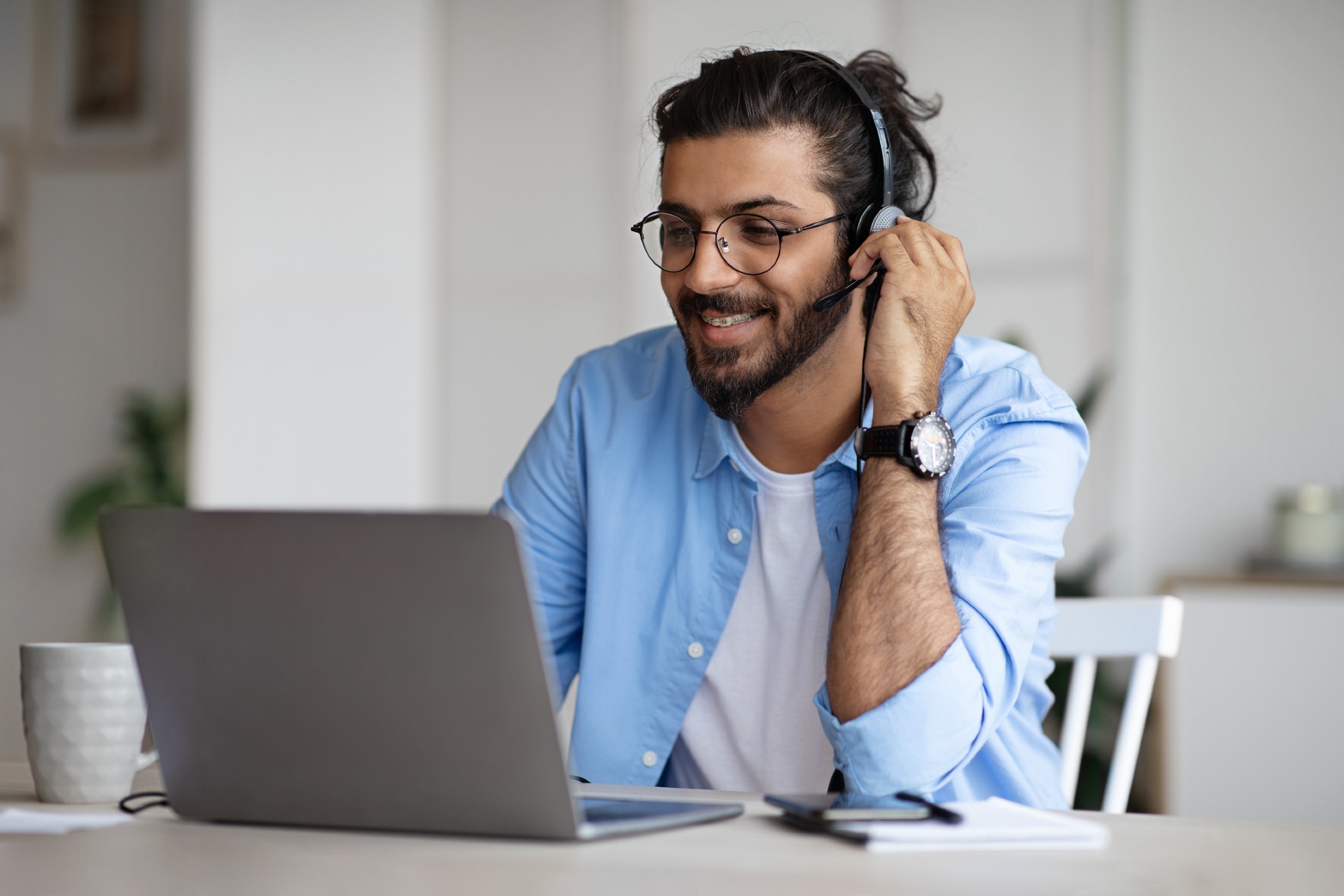 A man wearing a headset sits at a laptop