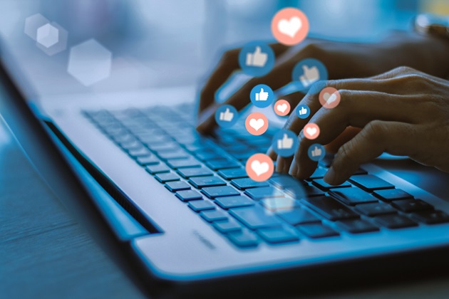 A person uses a laptop and social media graphics rise out of it to illustrate they are communicating online