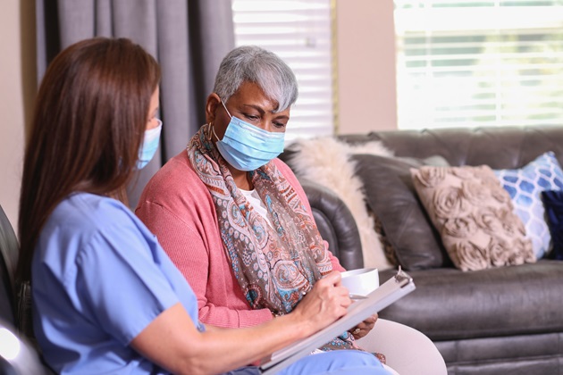 Community nurse wearing a mask talking to a patient wearing a mask in their home