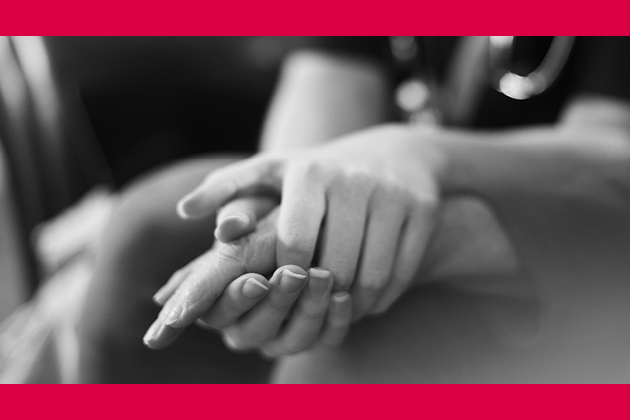 Black and white image with red border of nurse holding a patient's hand