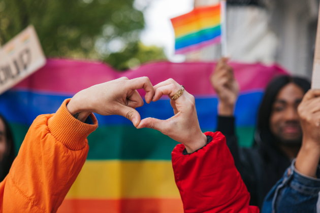 Two people create a heart symbol at Pride