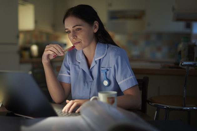 Nurse sitting in a darkened kitchen at a laptop
