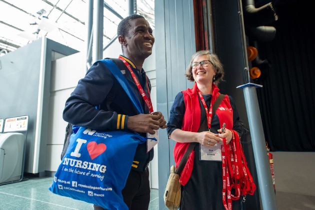 Smiling man carrying a bag with "I love nursing" on is greeted by a woman entering RCN Congress