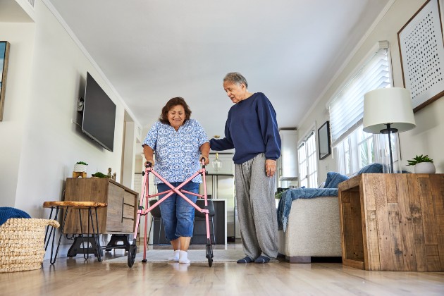 Woman using walking equipment in her home with a man stood next to her.